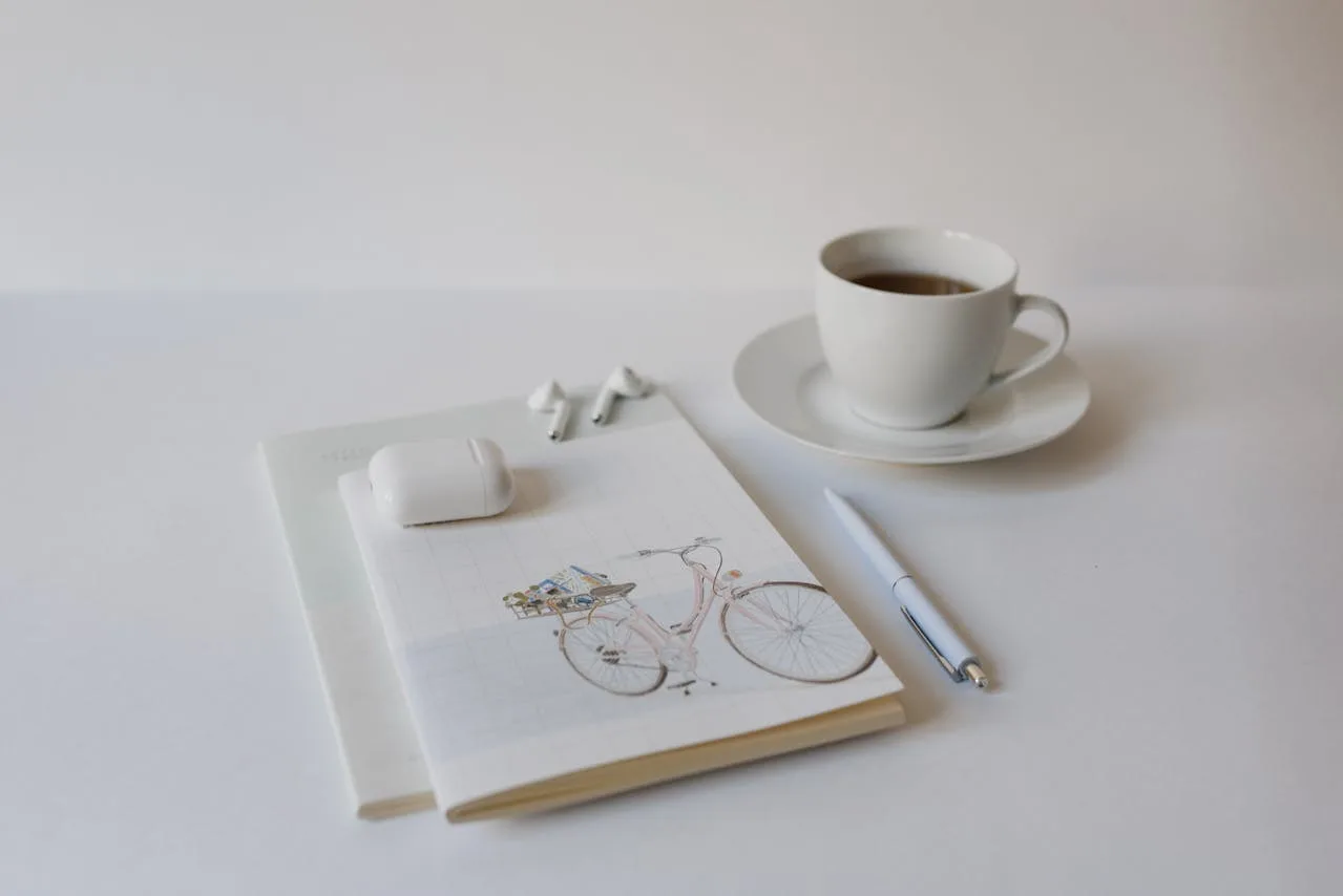 A cup of coffee beside an open notebook and pen on a white table