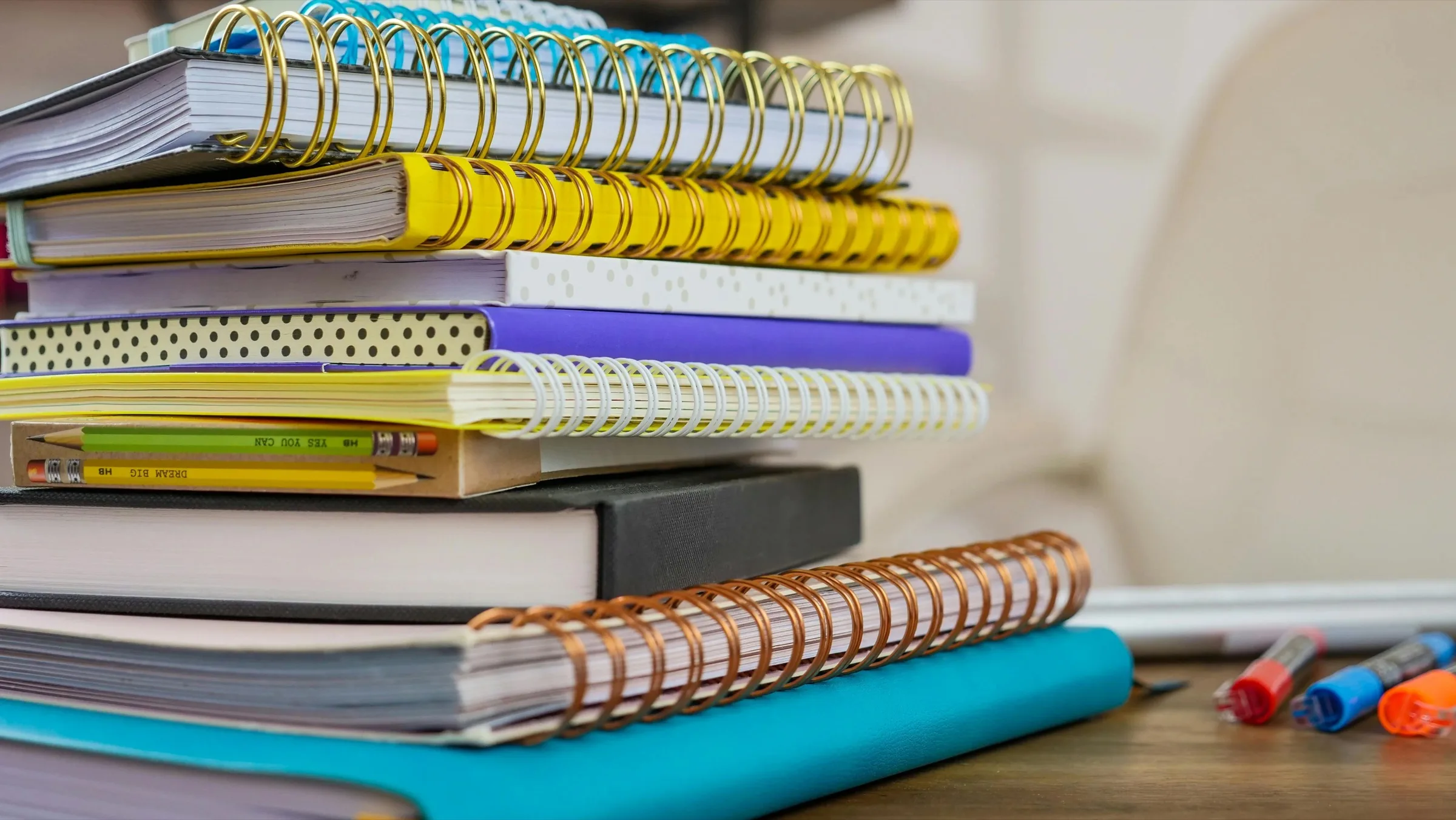 A stack of colorful spiral notebooks with pens on a desk