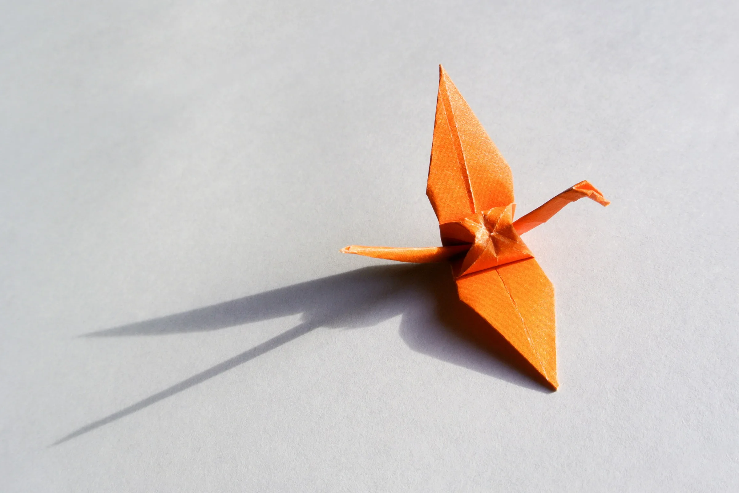 Orange origami bird on neutral background